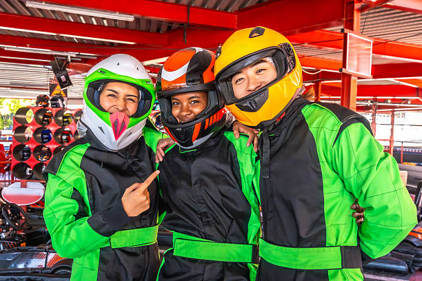 Three young adult friends wearing racing suits and helmets, smiling and enjoying a day of competitive go-karting on an indoor track, celebrating friendship and recreation