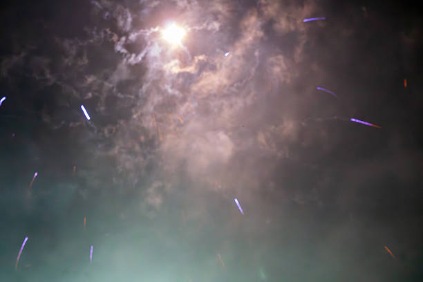 Abstract view of a smoky night sky illuminated by a bright light source and scattered light trails. Soft haze and drifting clouds create a mysterious atmospheric background.