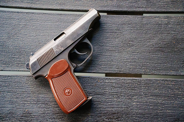 A small handgun is placed on a dark wooden surface. The setting appears to be indoors with good lighting. The focus is on the firearm.