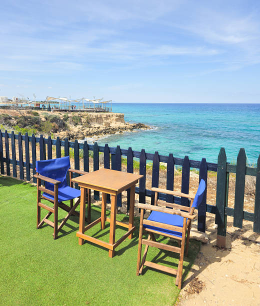 Outdoor table and chairs overlooking turquoise sea and rocky coastline under a bright blue sky. Protaras holiday resort, Cyprus