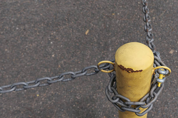 Part of the Quiet Urban Textures series, this image explores the subtle character of city surfaces through material, detail and atmosphere. Metal chain wrapped around a yellow post on asphalt ground, concept of restriction and boundary.