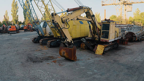 Rusty excavators and construction machinery parking in an industrial scrapyard during daytime