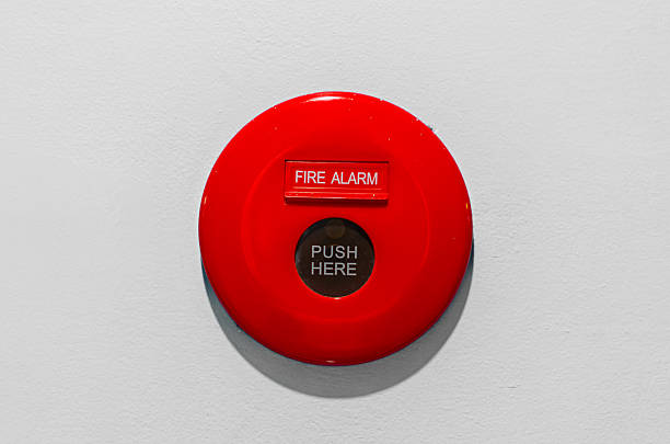fire alarm button is installed on the white plaster wall inside the building.