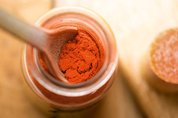 Close up of vibrant ground paprika inside a small glass jar, red spice powder used in cooking, food seasoning and culinary ingredient concept.