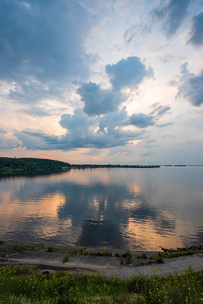 Dnieper river reflecting the colorful clouds of an evening sky with a distant green forest shoreline and a calm water surface creating a tranquil landscape in Ukraine