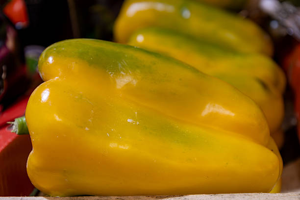 Closeup view of a glossy yellow bell pepper displayed at a market. The smooth surface and vibrant color highlight the freshness and natural quality of this healthy vegetable.
