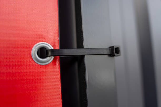 Close up of black strap fastener through metal grommet on red textured fabric panel, modern industrial securing mechanism detail with gray background