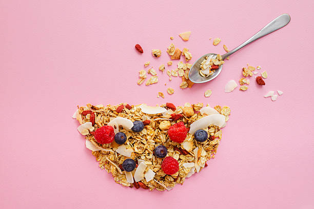 Healthy granola with fresh berries and coconut flakes on pink background