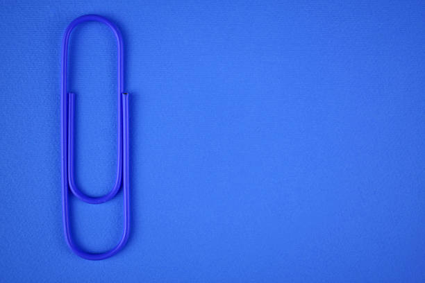 Paper clip of blue color on a blue background. Copy space.