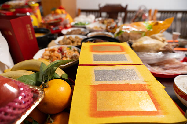 Yellow ceremonial joss paper stacks on dining table with oranges and traditional dishes during Chinese festival