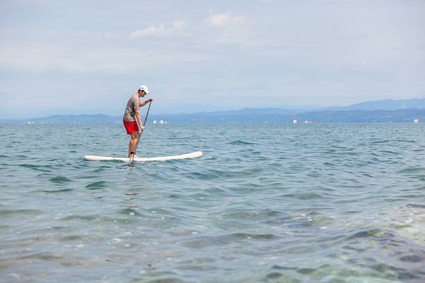A young man enjoys paddleboarding on the sea under the sun. He is active in a fun water sport on a summer day at the beach.