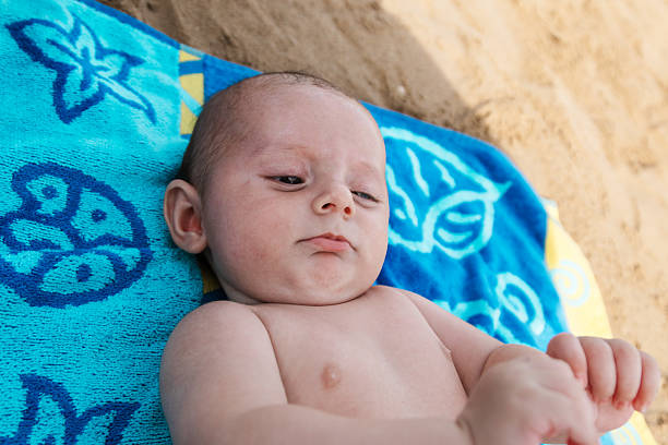 Baby lying on blue towel at the beach, soaking summer sun and sand in a peaceful, carefree outdoor moment of rest