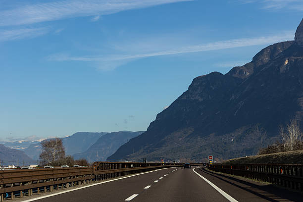 Scenic highway road leading through dramatic mountain landscape under a clear blue sky. Open asphalt road with guardrails and distant peaks creates a concept of travel, freedom, transportation and journey through nature.