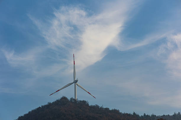 Modern wind turbine standing on a hill under dynamic cloudy sky. Clean renewable energy production and sustainable power generation concept.