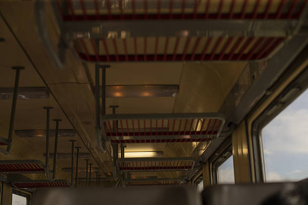 empty vintage train carriage with luggage racks, overhead metal shelves and rows of seats, warm interior lighting and window