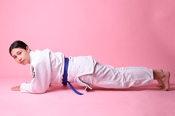 Profile shot of a teenager during a strength workout on a pink surface wearing a traditional uniform and blue belt