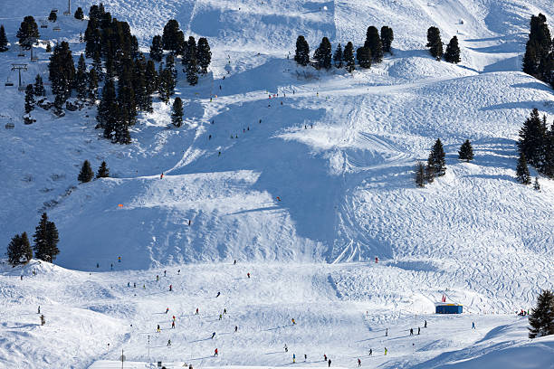 Snow covered mountain with ski slopes, skiers, ski lift and trees on a sunny day in Austrian Alps.