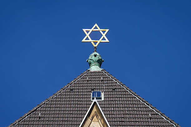 Close-up of the golden Star of David atop the Roonstrasse Synagogue against a clear blue sky, a symbol of Jewish life in Cologne, Germany