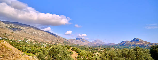 A wide hillside view from Crete, Greece, showing olive groves, terraced fields, and rugged mountains under a clear blue sky. The scene conveys rural calm, Mediterranean warmth, and timeless countryside charm, perfect for travel, nature, and scenery collections.