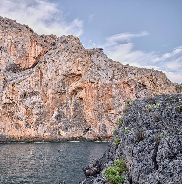 Crete Greece coastal cliffs rise from calm blue water under a bright sky. A rugged rock face this natural scene captures raw geology, sea, and solitude, evocative of outdoor exploration and travel in Greece.