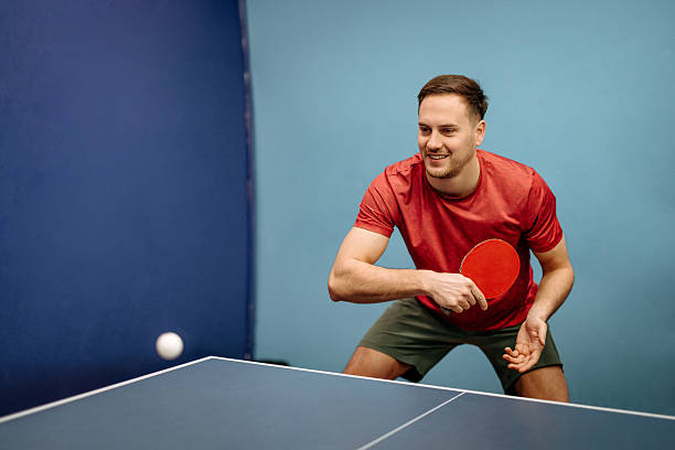 Smiling man plays table tennis, focused and active during a recreational or competitive game in an indoor sports setting.