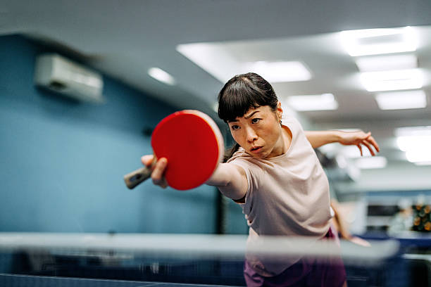 A focused woman plays ping pong, showcasing quick reflexes and hand-eye coordination.