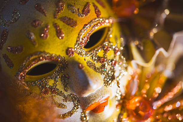 A gold mask with orange and gold decorations. The mask is on a table. The mask is very detailed and has a lot of glitter
