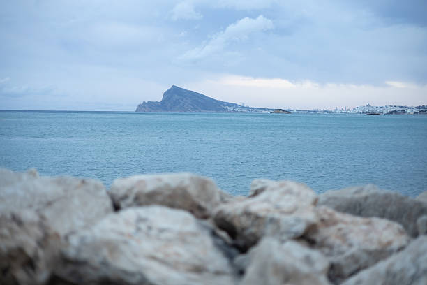 Serene ocean view with rocky shoreline and distant mountain under cloudy sky, peaceful coastal landscape for travel and nature themes