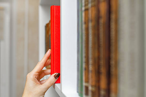 female picking red book from bookshelf, close-up. a woman's hand takes a red book from the shelf. hand takes a book, close-up.