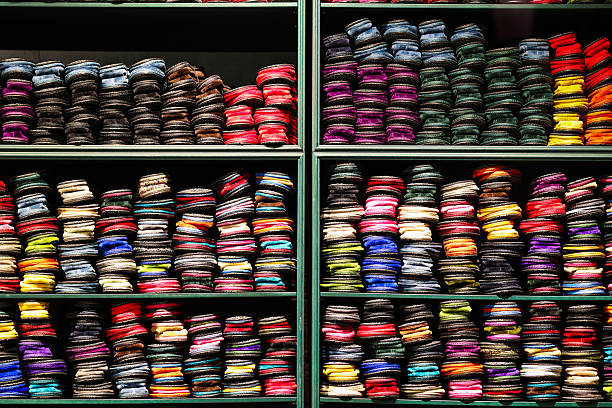 A vibrant display of neatly stacked fabric swatches arranged across retail shelves, showcasing a rich spectrum of colours and textures. The organised repetition and layered textiles create a striking visual pattern, ideal for themes of fashion design, interior styling, craft, tailoring and the creative industries.