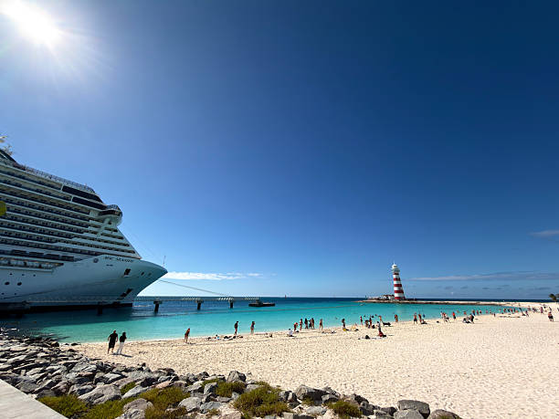 Ocean Cay, Bahamas - January 8, 2026: MSC Seaside large cruise ship docked at a tropical island beach in Ocean Cay, Bahamas, with people enjoying the turquoise water and white sand under a bright sunny sky, featuring a striped lighthouse