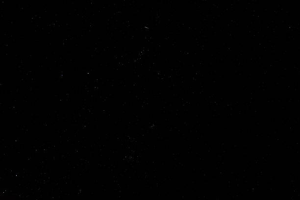 A bright meteor streaks across a clear starry night sky above a remote alpine landscape. The dark mountain silhouettes create a dramatic foreground beneath the vast cosmos filled with countless stars.