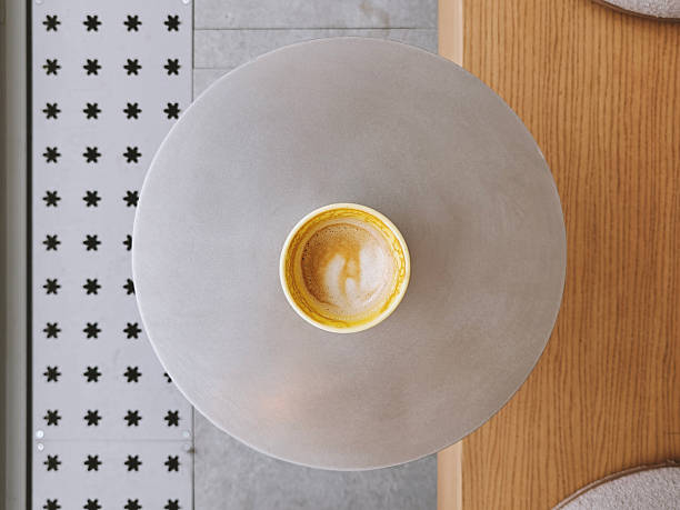 Yellow cup of latte or cappuccino that is already half-drunk on a metal round table in front of a bunch with soft cushions. Top view, copy space. Coffee shop, hot drink concept. Part of a series.