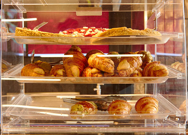 Display case filled with assorted pastries including croissants, cookies, and tarts in a bakery setting with warm lighting