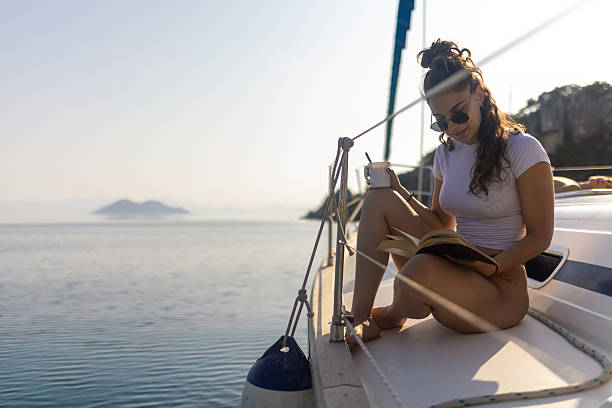 Young woman reading book on sailboat deck
