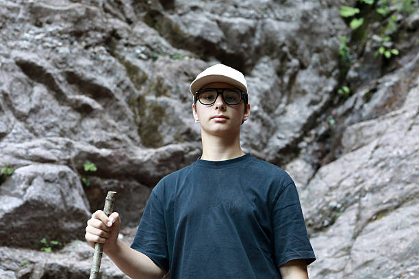 Young man posing with a stick against a natural rock face. Teenager exploring nature in a mountain gorge, ideal for travel and adventure themes.