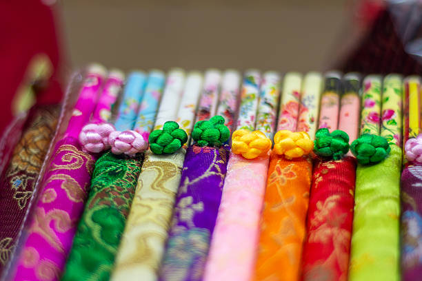 Colorful decorative chopsticks in Chinese silk in neat row with floral patterns and braided knots, shallow depth of field, vibrant traditional souvenir craft display.