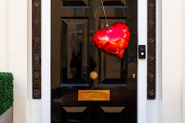 A black Victorian-style six-panel front door, which is a popular architectural element in London neighborhoods like Belgravia, Mayfair, and Notting Hill. The door is decorated with a single red heart-shaped foil balloon.