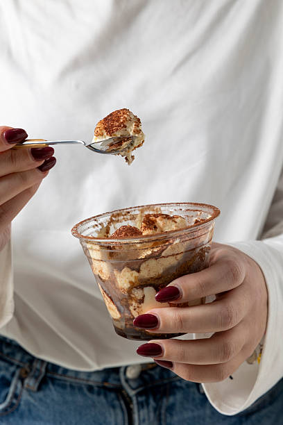 Person eating tiramisu dessert with a spoon from a cup