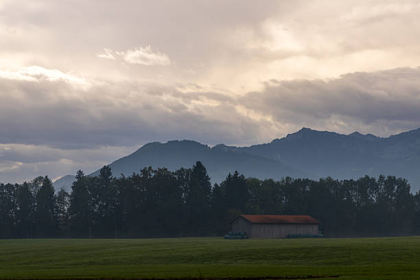Wolkengebilde über einer Landschaft mit Gebirge Wiesen Hütte