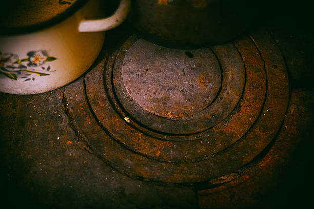 A rusty old stove with a worn vintage pot placed on top, creating a nostalgic and slightly moody still life. The scene conveys themes of abandonment, rural life, past times, decay and history, suitable for concepts such as old household equipment, forgotten places, survival, or vintage lifestyle.