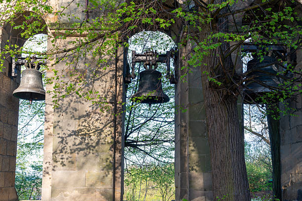 Trio of bronze bells mounted in a weathered stone structure, partially covered by fresh spring branches. Strong vertical composition for history, architecture, spirituality, and cultural heritage themes.