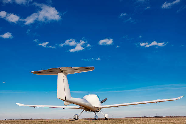 White light single-engine plane parked on a grassy runway beneath a bright blue sky, ready for flight — evokes travel, freedom, leisure and small-plane adventure
