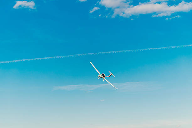 Small propeller plane soaring through a beautiful bright blue sky with wispy clouds and a fading contrail, representing concepts of travel, freedom, and adventure