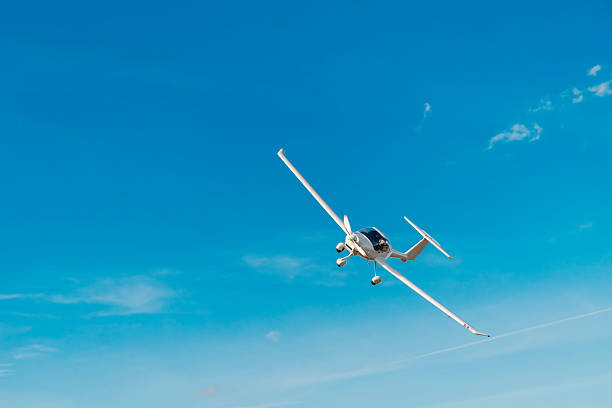 Small white propeller plane soaring across a bright blue sky with wispy clouds and contrail, conveying modern private aviation, freedom, adventure and open-air travel