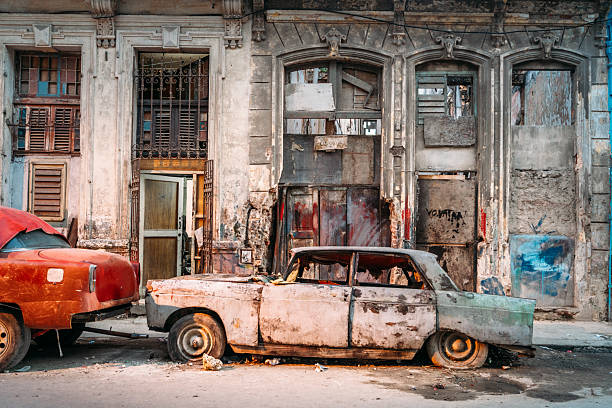 Weathered classic cars sit parked before a crumbling colonial facade in Havana, Cuba, evoking nostalgia, urban decay and vintage charm in a colorful, textured street scene popular with travelers.