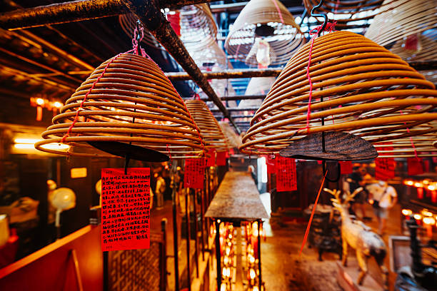 Warm, atmospheric interior of Man Mo Temple in Sheung Wan, Hong Kong, showing large spiral incense coils, red prayer tags and devotees honoring the gods of literature and martial arts.