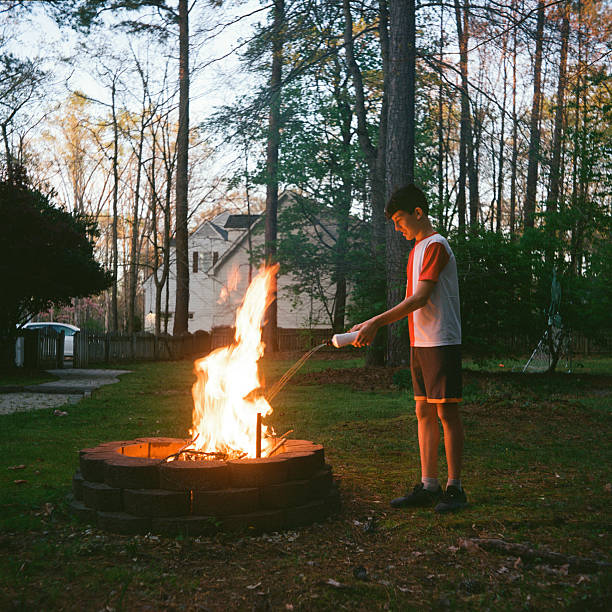 Teenage boy starting a fire in the pit with lighter fluid. Shot on film.
