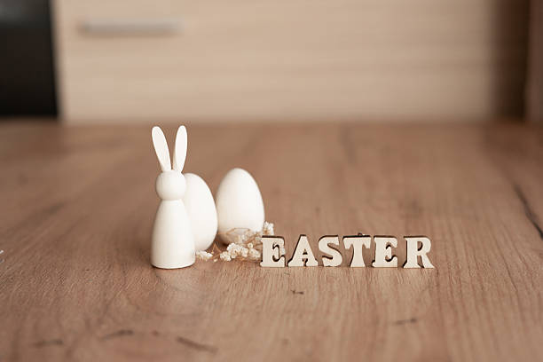 Minimal Easter still life on wooden floor with white bunny figurine, eggs and wooden letter blocks spelling easter, soft natural light, copy space. easter decor with bunny and eggs on wooden floor