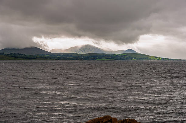 The sky is cloudy and the water is dark. The mountains in the background are covered in trees